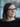 Woman with glasses smiling gently, with a blurred background.