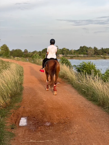 A rider moving along a quiet red-earth trail beside water at Vonfidel Ranch in Sri Lanka.