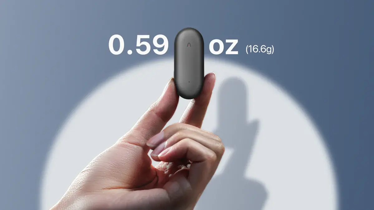 Устройство NotePin весом всего 16,6 г (0.59 oz), держится двумя пальцами на фоне тени.